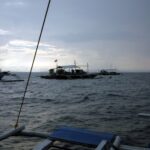 Tři potápěčské lodě banca na kotvě na Monad Shoal pod šedou ranní oblohou, viděné z paluby jiné lodi