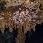 Hnědobílý vápencový strop posetý krátkými stalaktity, nasvícený svítilnou, v kaverně Dos Ojos