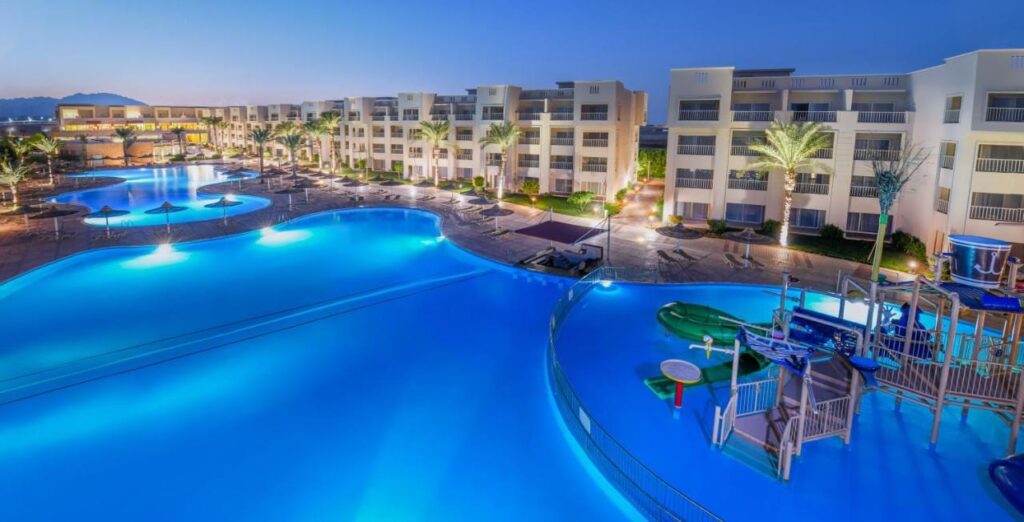 Osvětlené bazény hotelu JAZ Soma Beach za soumraku, mezi budovami a palmami