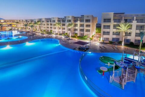 Osvětlené bazény hotelu JAZ Soma Beach za soumraku, mezi budovami a palmami