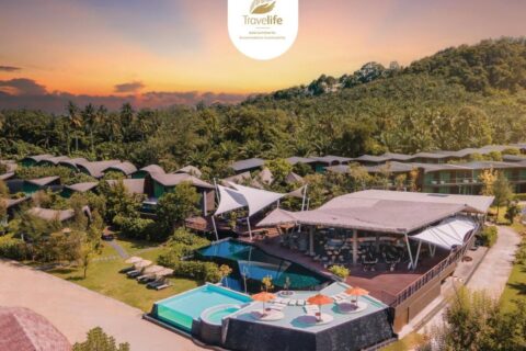 Letecký pohled na Kalima Resort Khao Lak při západu slunce, s bazény a zaoblenými střechami pod zalesněným kopcem
