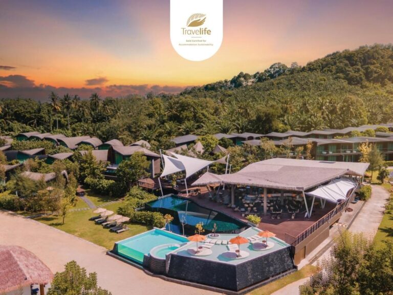Letecký pohled na Kalima Resort Khao Lak při západu slunce, s bazény a zaoblenými střechami pod zalesněným kopcem
