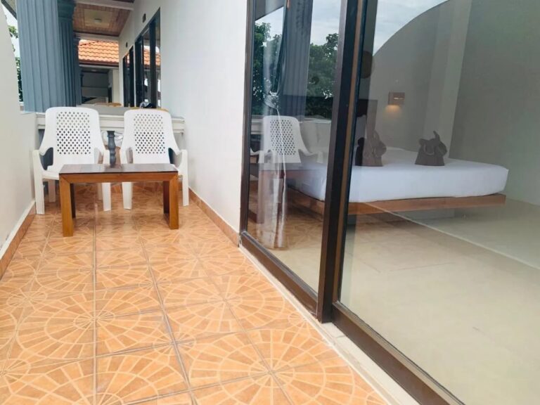 Dlážděný balkon se dvěma bílými židlemi a konferenčním stolkem před prosklenou stěnou pokoje