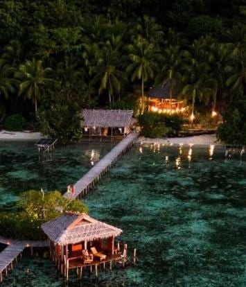 Letecký pohled na Nyande Raja Ampat za soumraku, s bungalovem na kůlech a molem vedoucím k pláži