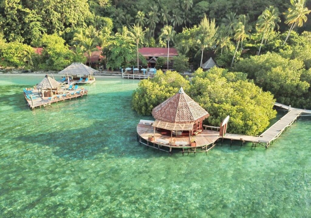 Letecký pohled na Raja Ampat Dive Lodge, jeho mola na kůlech a červené střechy pod palmami