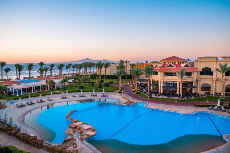 Velký bazén v Rixos Sharm El Sheikh při západu slunce, před palmami a horami Sinaje