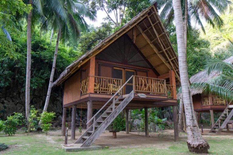 Bungalov na kůlech v Sangat Island Dive Resort s dřevěným schodištěm, pod palmami