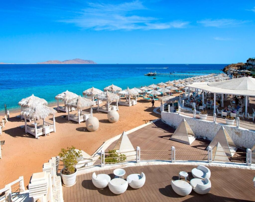 Pláž Sunrise Arabian Beach Resort se slaměnými slunečníky a molem, naproti ostrovu Tiran