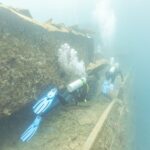 Dva potápěči plavou podél paluby vraku Thistlegorm u chodby, v mléčně modré vodě